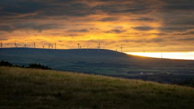 atmospheric sunset over a wind farm with clouds and hill