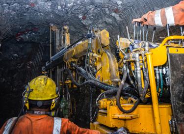 workers wearing safety clothing and helmets working with machiney in a mine