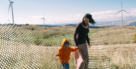 A mother and child walking through a nature reserve with wind turbines in the background